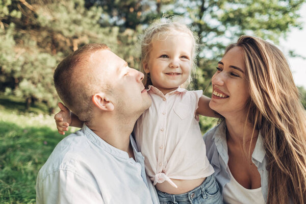 Young Adult Couple with Their Little Daughter Having Fun in the Park Outside the City, Family Weekend Picnic Concept, Three People Enjoying Summer