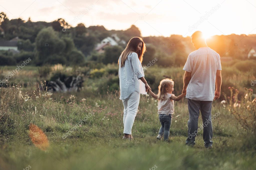 Young Adult Couple with Their Little Daughter Having Fun in the Park Outside the City, Family Weekend Picnic Concept, Three People Enjoying Summer