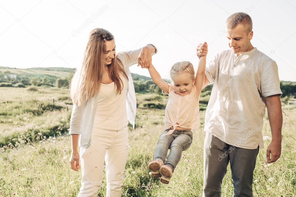 Young Adult Couple with Their Little Daughter Having Fun in the Park Outside the City, Family Weekend Picnic Concept, Three People Enjoying Summer