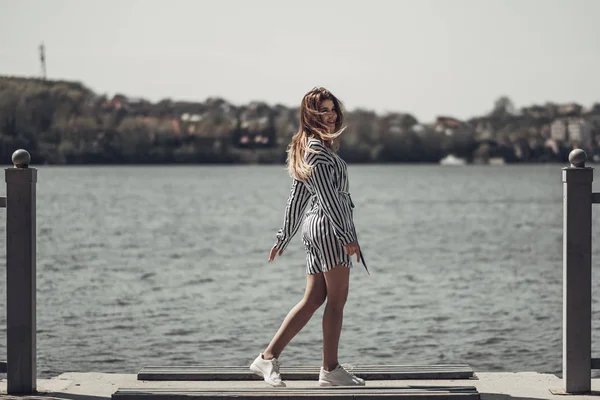湖に対する白いストライプのスタイリッシュなドレスで若い美しい女の子の屋外夏の肖像画 — ストック写真