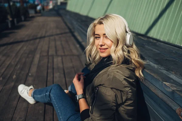 Menina loira bonita em Green Jacket ouvir música em fones de ouvido — Fotografia de Stock