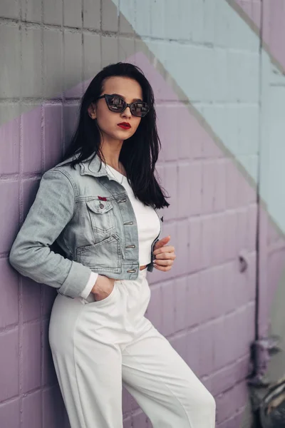Vacker brunett flicka i solglasögon vita byxor och jeans jacka, rött läppstift — Stockfoto