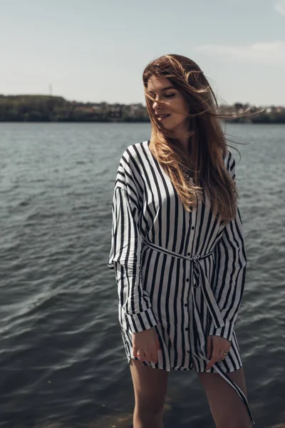 Retrato de verão ao ar livre de menina bonita jovem em branco listrado vestido elegante contra o lago — Fotografia de Stock