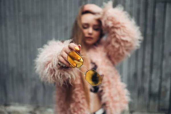 Close-up portret van een stijlvolle meisje in roze vacht en moderne gele zonnebril poseren op straat — Stockfoto