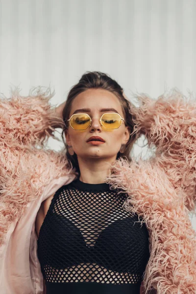 Fermer Portrait d'une fille élégante en manteau rose et lunettes de soleil jaunes modernes posant sur la rue — Photo