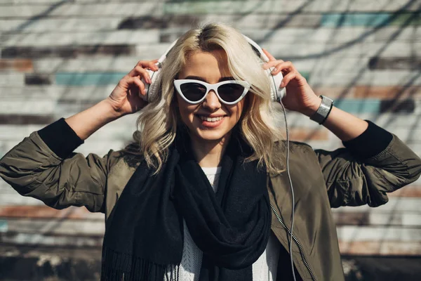 Beautiful Blonde Girl in Green Jacket Listening Music in Headphones — Stock Photo, Image