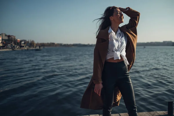 Hermosa joven con estilo chica de abrigo caminando en la playa de primavera al atardecer —  Fotos de Stock