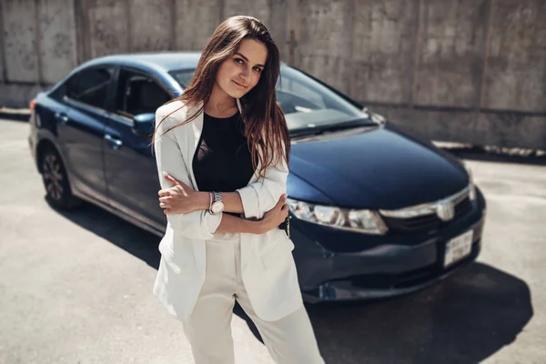 Moda elegante menina em terno branco posando perto do carro azul e detém chaves na mão — Fotografia de Stock