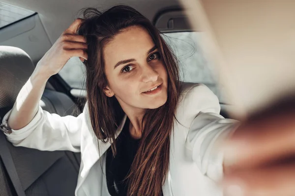 Moda elegante chica en traje blanco hace selfie en el coche — Foto de Stock