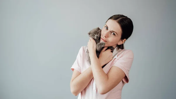 スタジオポートレートの若い大人のプリティーガールドレスでピンクのTシャツハグ彼女の小さなスコットランドの折り畳み猫 — ストック写真