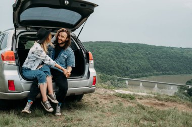 Genç, Şık Gezgin Hippiler, Nehir Kanyonu Seyahat ve Yolculuk Konsepti 'nin yanındaki Araba Bagajında Eğleniyor.