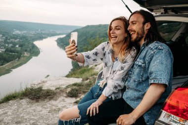 Modern arabada oturup Selfie, Seyahat ve Yolculuk Konsepti yaparak eğlenen genç ve şık bir çift.