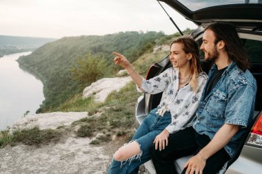 Genç, Şık Gezgin Hippiler, Nehir Kanyonu Seyahat ve Yolculuk Konsepti 'nin yanındaki Araba Bagajında Eğleniyor.