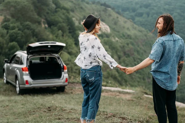 Young Trendy Traveling Couple Having Fun Near the Car on Top of Hill Travel and Road Trip Concept