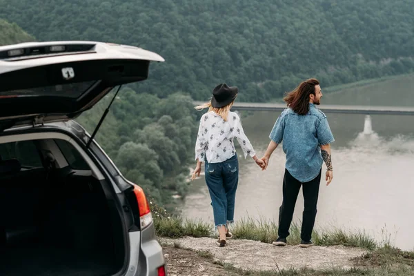 Young Trendy Traveling Couple Having Fun Near the Car on Top of Hill Travel and Road Trip Concept