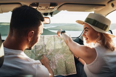 Happy Young Couple Sitting Inside Their Car Man and Woman Using Map on Road Trip, Travel and Adventure Concept clipart