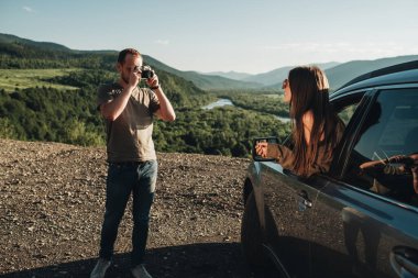 Genç Gezgin Çift Yolculukta, Erkek Kadının Güzel Manzara Üzerinde Arabalarıyla Keyifli Yolculuk Fotoğrafı Çekiyor