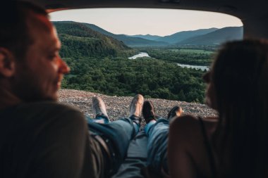Arabalarının bagajında yatan ve Horizon 'daki yolculuğun, dağların ve nehrin tadını çıkaran mutlu çiftin arka görüntüsü.