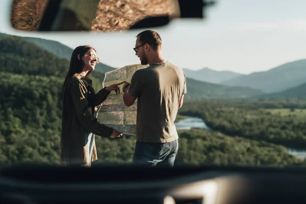 Traveler Couple on Road Trip, Man and Woman Using Map on Journey Near Their Car Over Beautiful Landscape