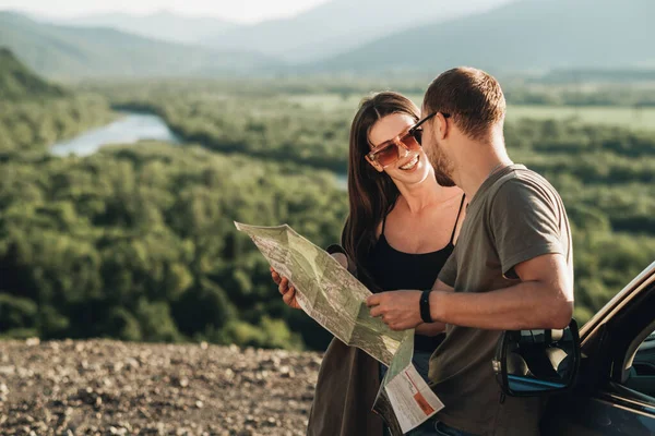 Travelers Couple on Road Trip, Man and Woman Using Map on Journey Near Their Car Over Beautiful Landscape