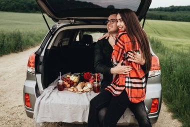 Araba bagajında oturan ve yolculuğun tadını çıkaran genç ve güzel bir çift, piknik konsepti.