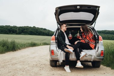 Araba bagajında oturan ve yolculuğun tadını çıkaran genç ve güzel bir çift, piknik konsepti.