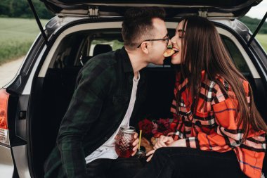 Araba bagajında oturan ve yolculuğun tadını çıkaran genç ve güzel bir çift, piknik konsepti.