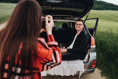 Genç ve güzel bir çift arabanın yanında eğlenirken kız sevgilisinin fotoğraflarını çekiyor.