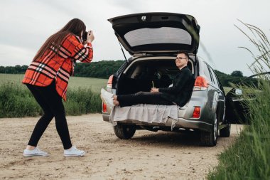 Genç ve güzel bir çift arabanın yanında eğlenirken kız sevgilisinin fotoğraflarını çekiyor.