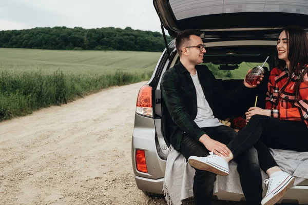 Araba bagajında oturan ve yolculuğun tadını çıkaran genç ve güzel bir çift, piknik konsepti.