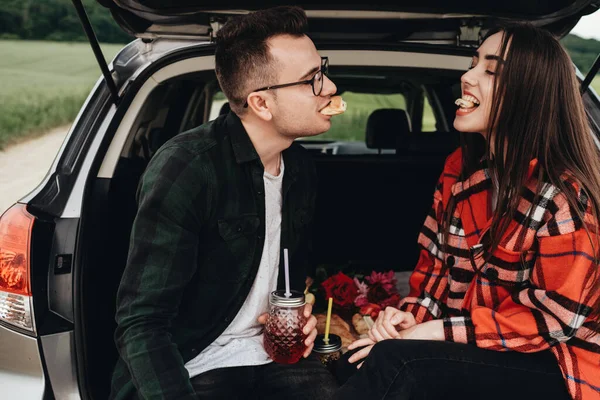 Araba bagajında oturan ve yolculuğun tadını çıkaran genç ve güzel bir çift, piknik konsepti.