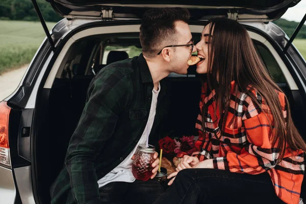 Araba bagajında oturan ve yolculuğun tadını çıkaran genç ve güzel bir çift, piknik konsepti.