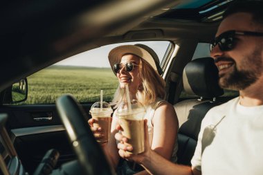 Kadın ve erkek arabada oturuyor, soğuk kahve içiyor ve macera yolculuğunun tadını çıkarıyorlar.