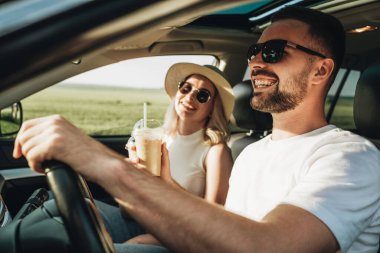Kadın ve erkek arabada oturuyor, soğuk kahve içiyor ve macera yolculuğunun tadını çıkarıyorlar.