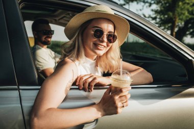 Kadın ve erkek arabada oturuyor, soğuk kahve içiyor ve macera yolculuğunun tadını çıkarıyorlar.