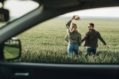 Erkek ve kadın zeytin ceketli giyinmiş, arabanın yanında eğleniyor, macera yolculuğunun tadını çıkarıyorlar.