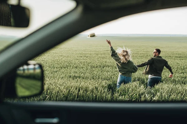 Erkek ve kadın zeytin ceketli giyinmiş, arabanın yanında eğleniyor, macera yolculuğunun tadını çıkarıyorlar.