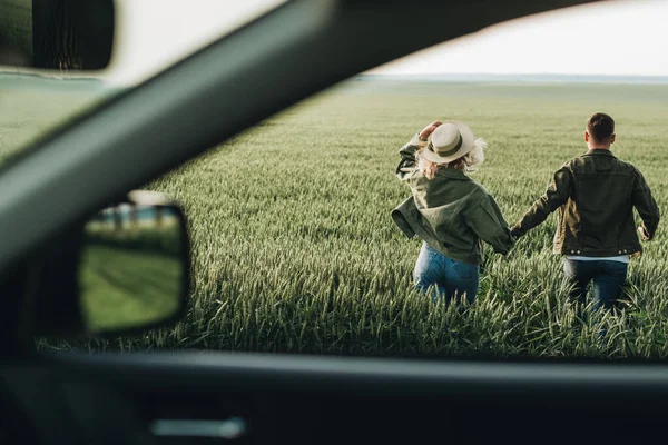 Erkek ve kadın zeytin ceketli giyinmiş, arabanın yanında eğleniyor, macera yolculuğunun tadını çıkarıyorlar.