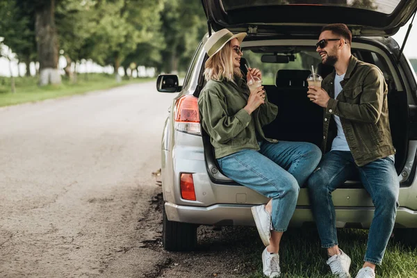 Kadın ve erkek, arabanın bagajında oturup soğuk kahve içiyorlar.