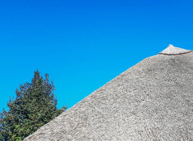 Mavi gökyüzüne karşı sazdan çatı. Mavi gökyüzünün altında eski geleneksel ahır veya baraka.