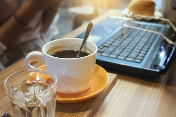 ถ้วยกาแฟและแล็ปท็อปบนโต๊ะไม้ในร้านกาแฟ — ภาพถ่ายสต็อก