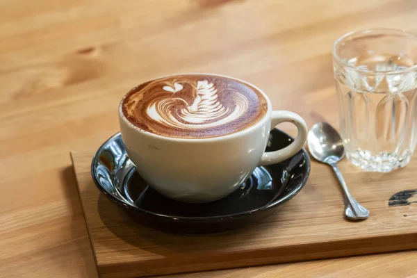 Secangkir kopi dengan seni Latte yang indah dengan air di atas meja — Stok Foto