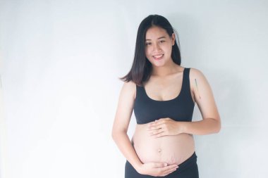 Gülümseyen hamile kadın ayakta ve karnını tutuyor..