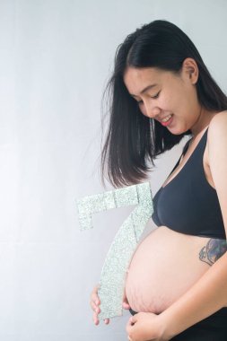 Ayakta ve karnını tutarak gülümseyen hamile kadın. 7 aylık hamile.