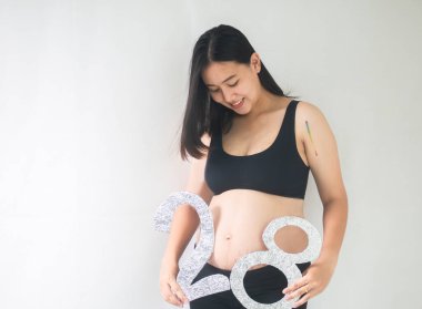 Beyaz arka planda duran gülümseyen hamile kadın. 28 haftalık hamile.