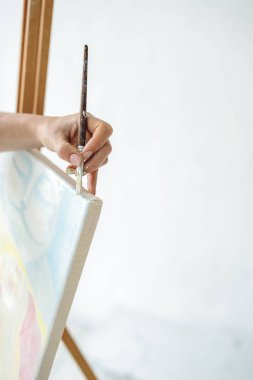 Siyah elbiseli ve önlüklü genç bir kadın parlak bir odada oturur ve resim yapar, yağlı boyaları Malbert 'le birlikte tuvale sürer.