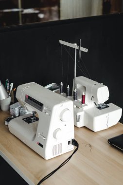 Terzinin masasında iki beyaz dikiş makinesi var.