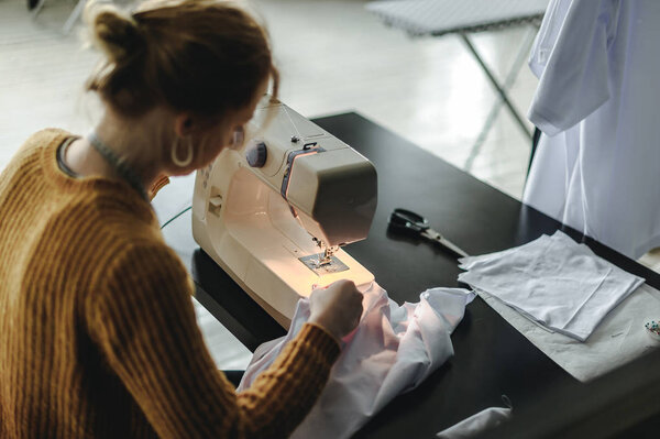 seamstress at work. woman working on a sewing machine, sitting at a table, sewing clothes, cloth