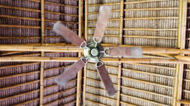 Dönen tavan vantilatörüne beş ahşap bıçakla örülmüş bir sap ve bambu kiriş tavanı, tropikal kulübe titreşimlerini ve doğal havalandırmayı yakalıyor.