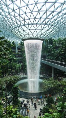 İnci, Singapur Changi Havalimanı, Singapur - 16 Ağustos 2025: dünyanın en uzun kapalı şelalesi olan Yağmur Girdabı 'nın dikey fotoğrafı, yağmur ormanları ağaçlarıyla çevrili ve yanında trenle yan yana.